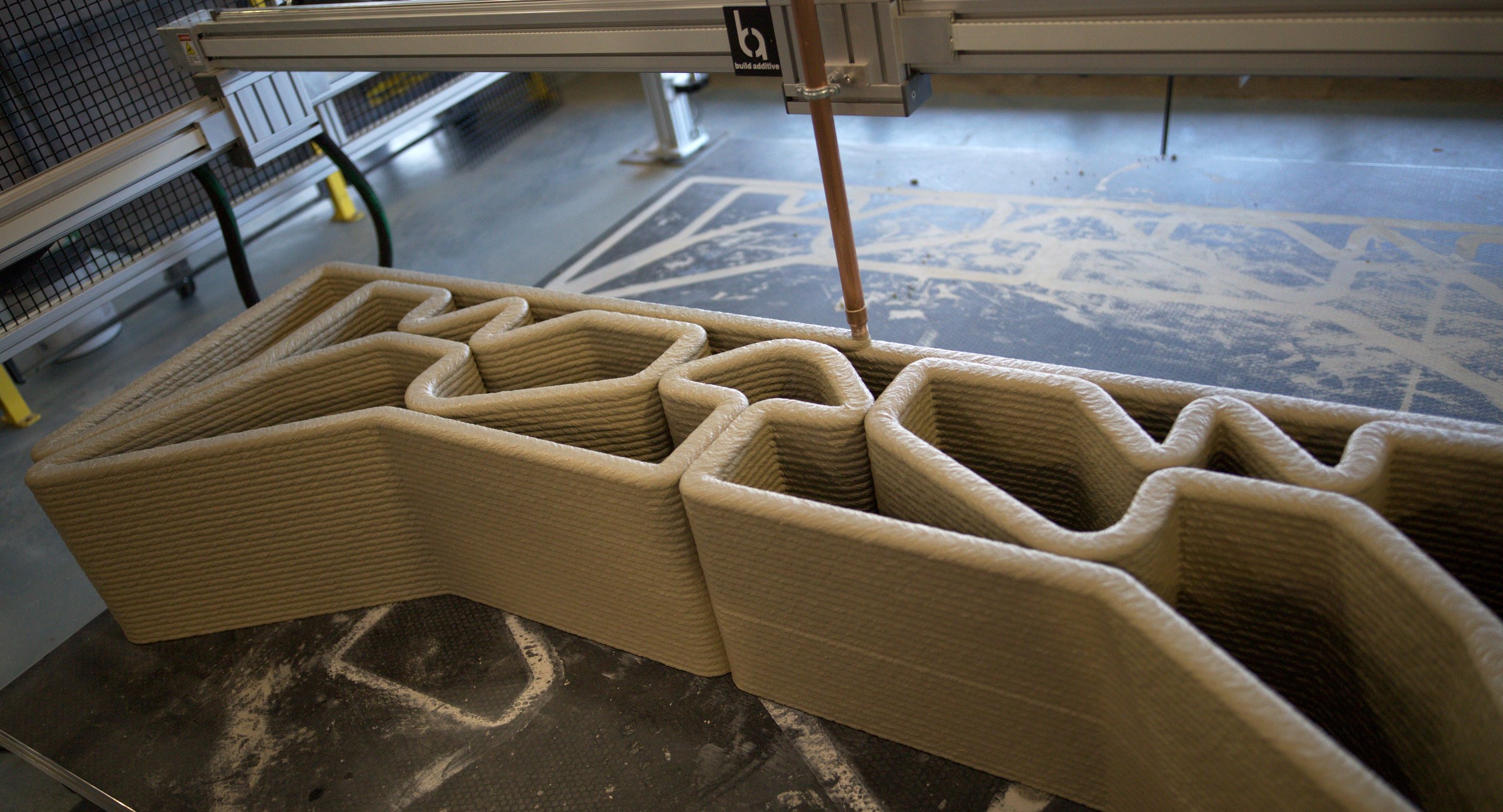 A parametrically optimized concrete beam being printed, with the Build Additive nozzle carriage above it