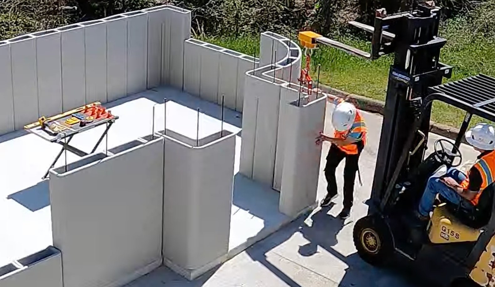 A crew setting factory-printed wall panels on a slab with a forklift and hoist